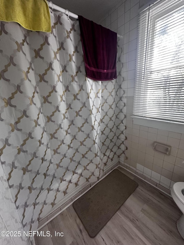 bathroom with toilet, tiled shower, tile walls, and wood finished floors