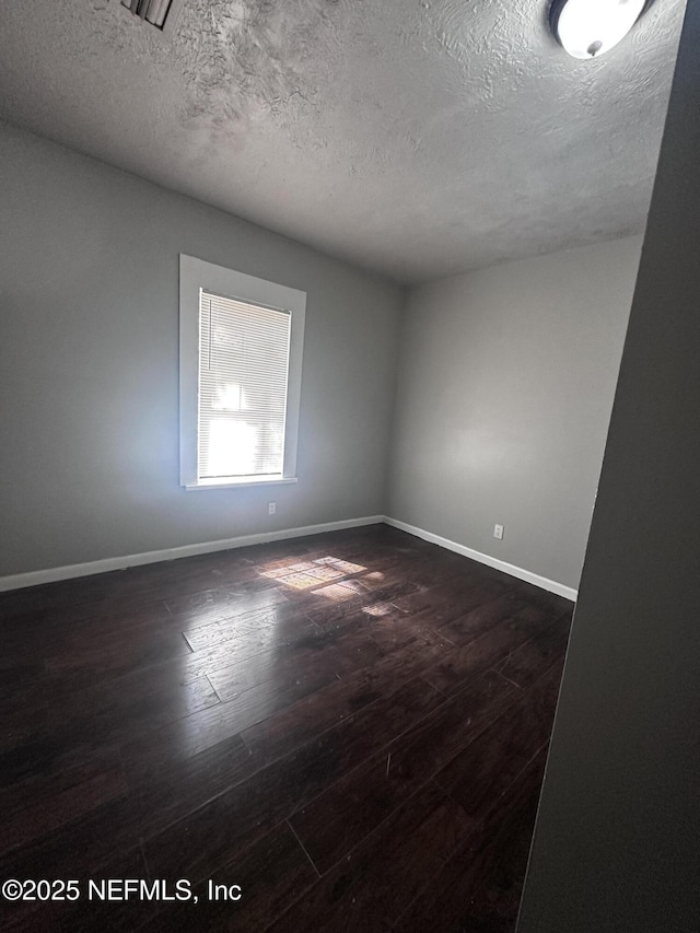 empty room with a textured ceiling, dark wood-style flooring, and baseboards