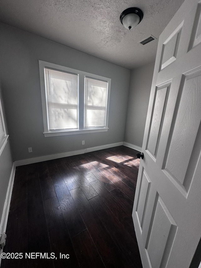 unfurnished bedroom featuring a textured ceiling, dark wood-style flooring, visible vents, and baseboards