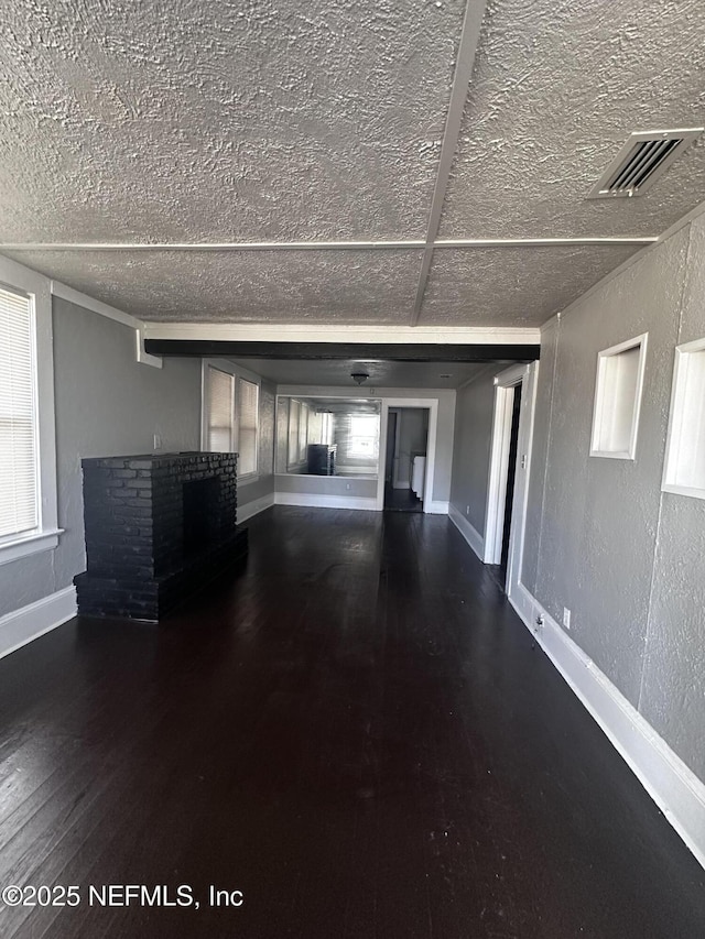 unfurnished living room featuring a fireplace, visible vents, a textured wall, hardwood / wood-style floors, and baseboards