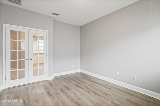 empty room featuring light wood-type flooring, a textured ceiling, and french doors