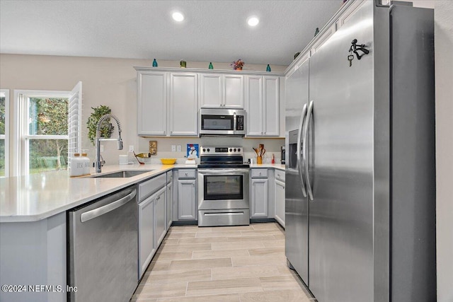 kitchen featuring kitchen peninsula, sink, a textured ceiling, appliances with stainless steel finishes, and light wood-type flooring