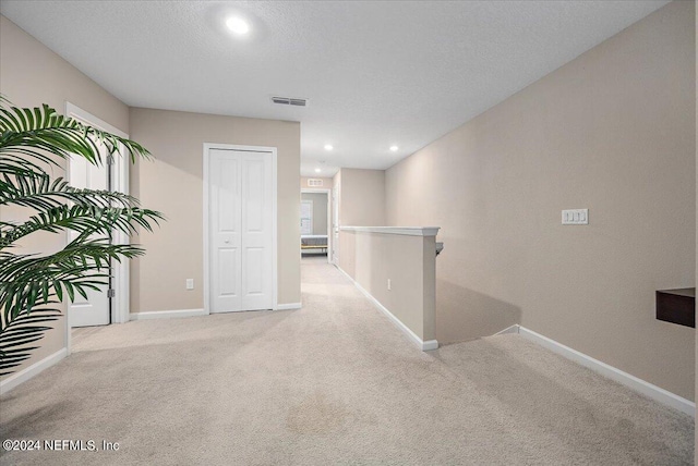 corridor featuring a textured ceiling and light colored carpet