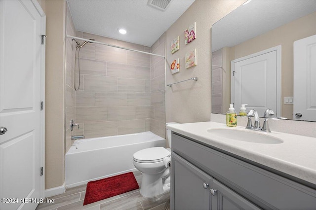 full bathroom featuring vanity, tiled shower / bath combo, toilet, and a textured ceiling