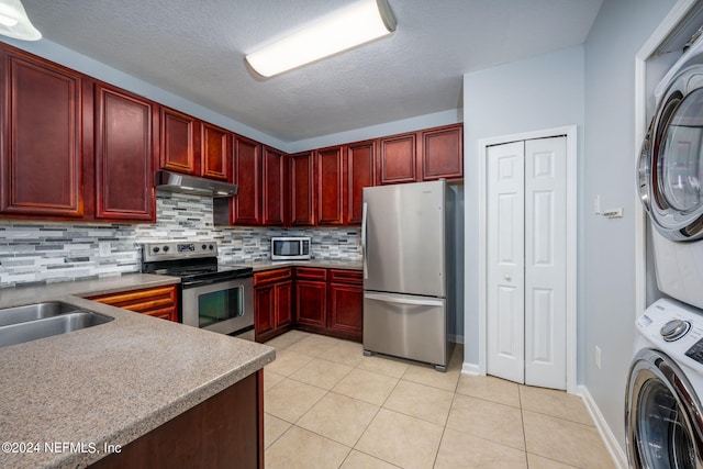 kitchen featuring light tile patterned floors, a textured ceiling, backsplash, stacked washing maching and dryer, and stainless steel appliances