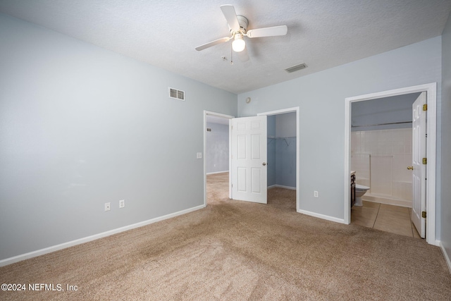 unfurnished bedroom featuring a closet, ensuite bath, carpet, a spacious closet, and ceiling fan