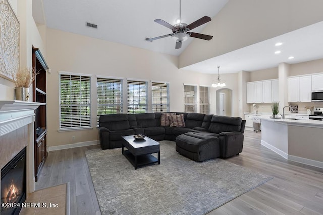 living room with ceiling fan with notable chandelier, high vaulted ceiling, and light hardwood / wood-style floors