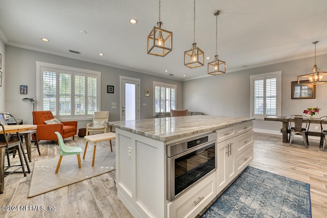 kitchen with decorative light fixtures, white cabinetry, a center island, light hardwood / wood-style floors, and a healthy amount of sunlight