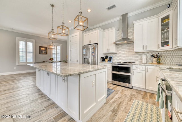 kitchen featuring pendant lighting, white cabinets, wall chimney exhaust hood, stainless steel appliances, and ornamental molding