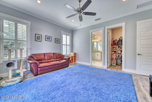 living room with ornamental molding, light hardwood / wood-style floors, ceiling fan, and a textured ceiling