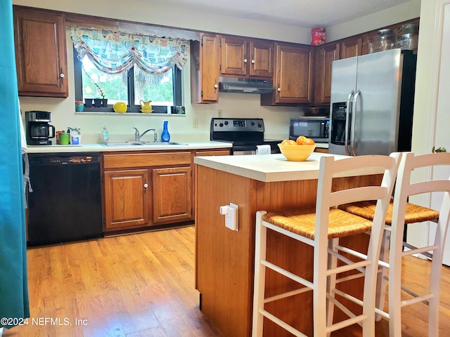 kitchen with black appliances, light hardwood / wood-style floors, sink, and a breakfast bar area