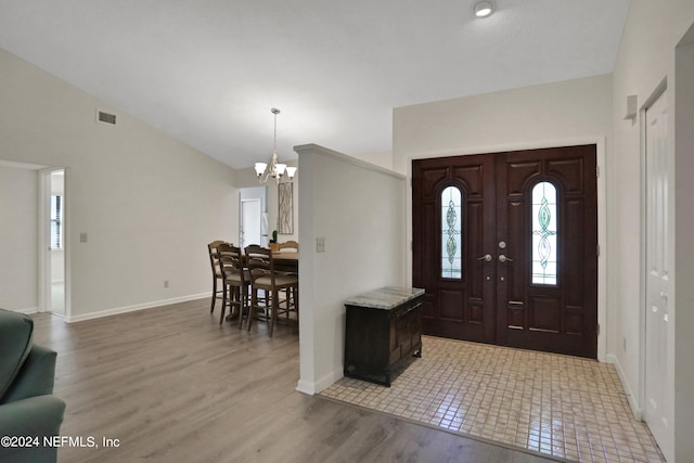 foyer entrance featuring an inviting chandelier, wood-type flooring, and vaulted ceiling