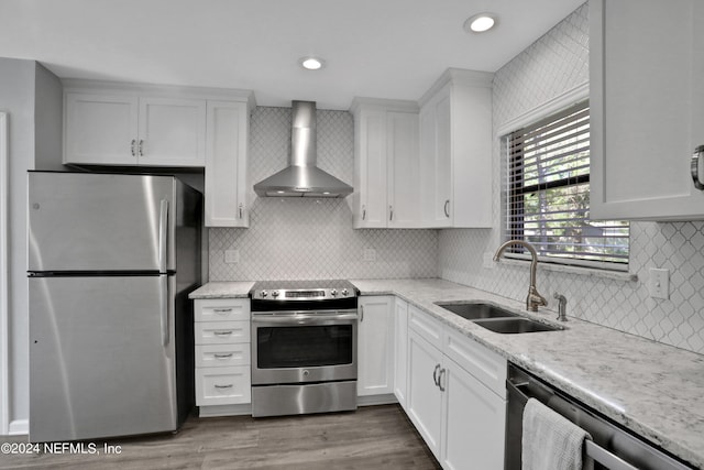 kitchen featuring stainless steel appliances, white cabinetry, wall chimney range hood, and sink