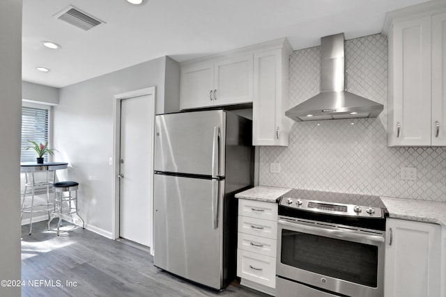 kitchen with appliances with stainless steel finishes, white cabinetry, light stone countertops, hardwood / wood-style floors, and wall chimney range hood