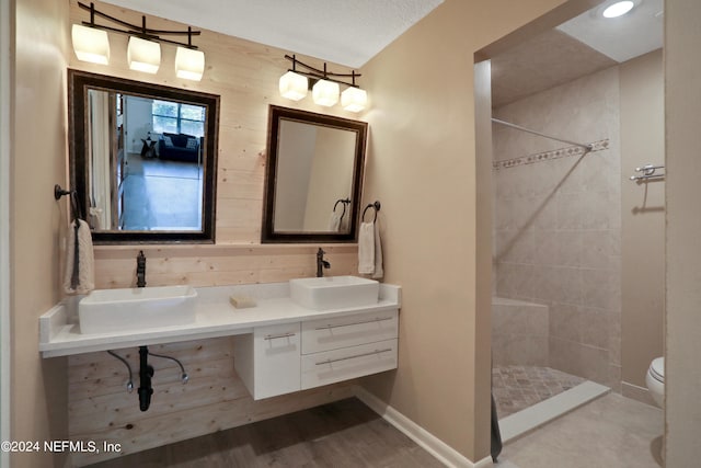 bathroom featuring a tile shower, a textured ceiling, wood walls, vanity, and toilet