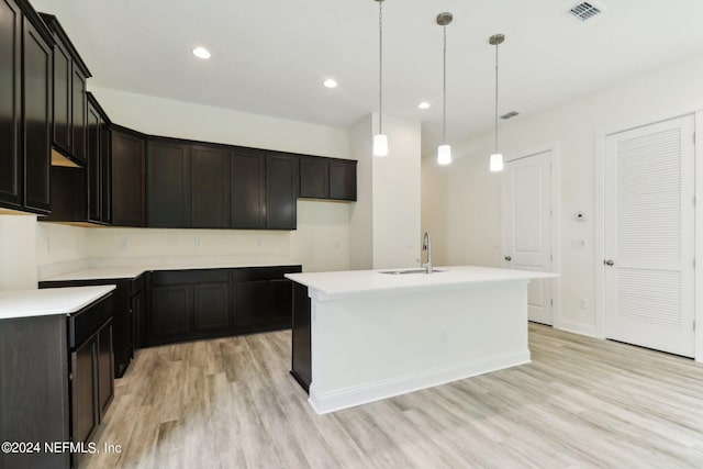 kitchen with an island with sink, light wood-type flooring, hanging light fixtures, and sink