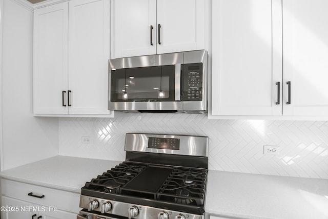 kitchen with appliances with stainless steel finishes, light countertops, white cabinets, and backsplash