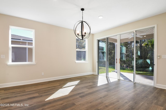 unfurnished dining area with dark wood-style floors, an inviting chandelier, and baseboards