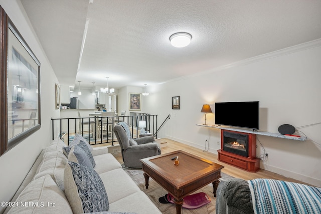 living room with light wood-type flooring, crown molding, a textured ceiling, and a notable chandelier