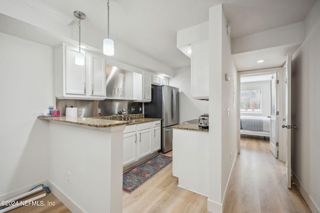 kitchen with stainless steel fridge, decorative light fixtures, light hardwood / wood-style flooring, and white cabinets