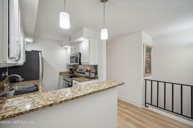 kitchen with white cabinets, hanging light fixtures, sink, kitchen peninsula, and stainless steel appliances