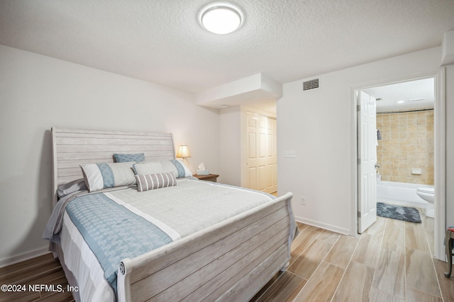 bedroom with light hardwood / wood-style flooring, ensuite bath, and a textured ceiling