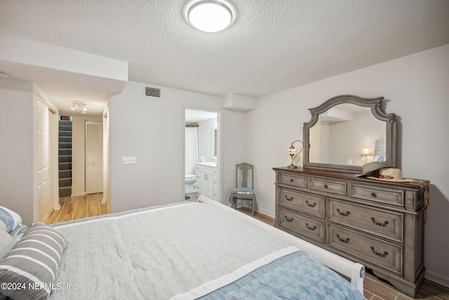 bedroom with connected bathroom, light hardwood / wood-style floors, and a textured ceiling