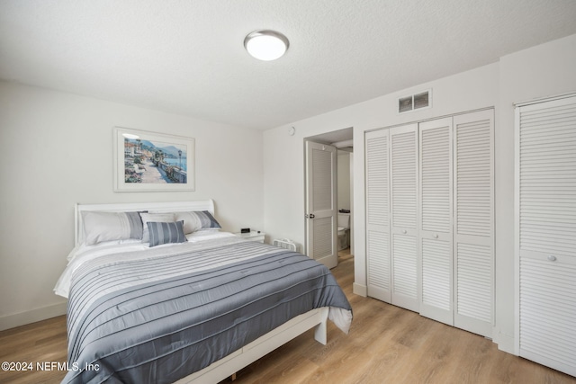 bedroom featuring light wood-type flooring, a textured ceiling, and multiple closets