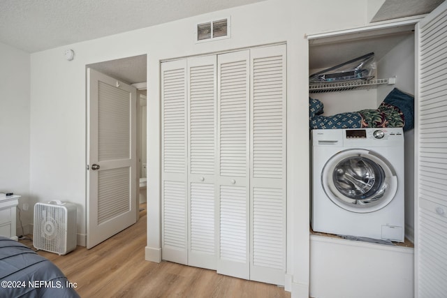 laundry area with light wood-type flooring, a textured ceiling, and washer / clothes dryer