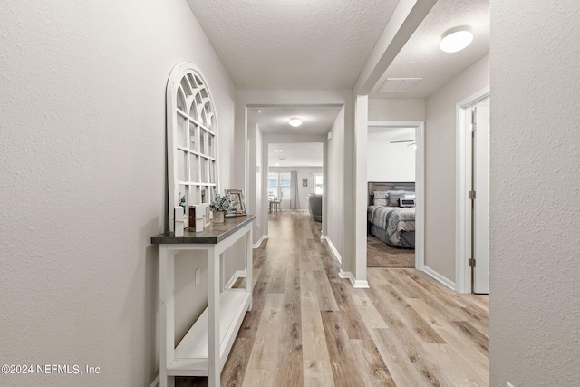 hallway featuring light wood-type flooring and a textured ceiling