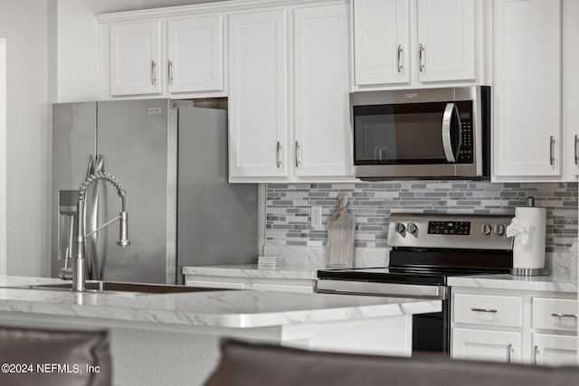 kitchen with light stone countertops, appliances with stainless steel finishes, backsplash, and white cabinetry