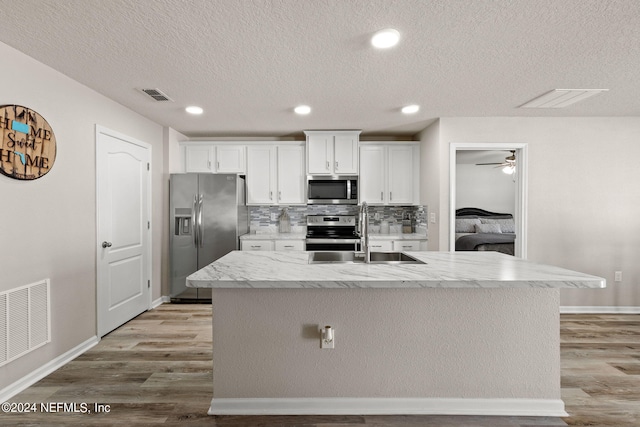 kitchen featuring sink, white cabinets, light hardwood / wood-style flooring, stainless steel appliances, and a center island with sink