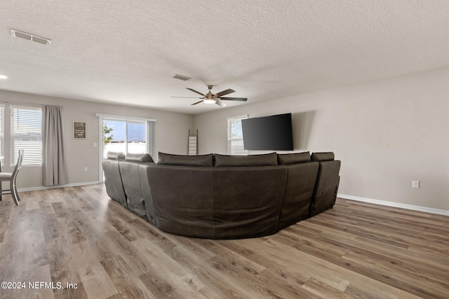 living room with light hardwood / wood-style floors, ceiling fan, and a textured ceiling