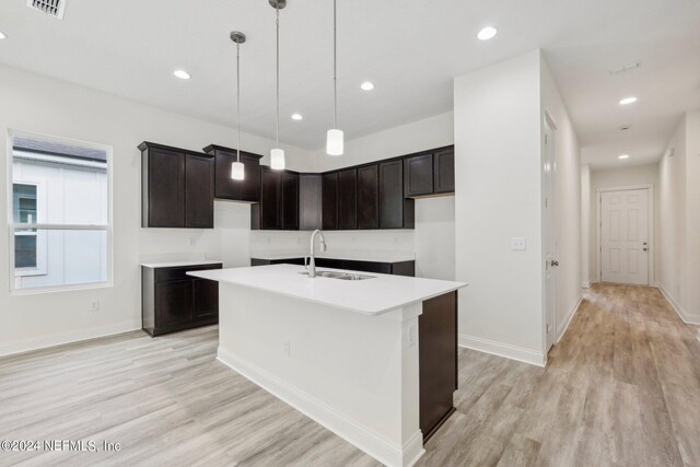 kitchen featuring dark brown cabinetry, pendant lighting, an island with sink, sink, and light wood-type flooring