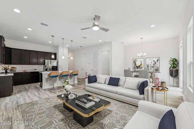 living room featuring ceiling fan with notable chandelier and light hardwood / wood-style flooring