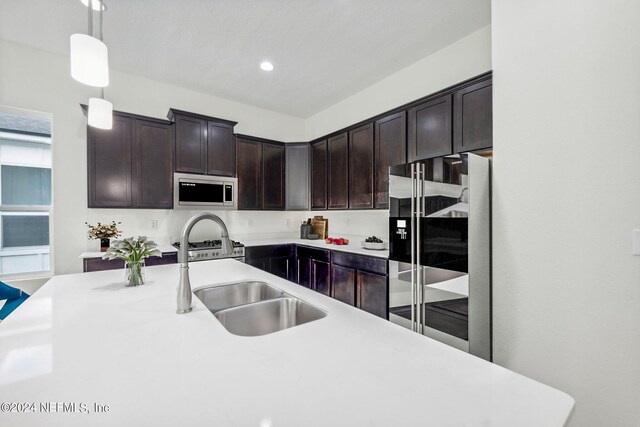 kitchen featuring stainless steel appliances, dark brown cabinetry, decorative light fixtures, and sink