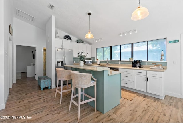 kitchen featuring pendant lighting, light hardwood / wood-style floors, a center island, white cabinets, and vaulted ceiling