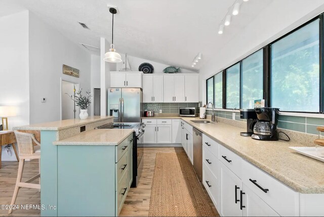 kitchen with vaulted ceiling, white cabinets, pendant lighting, stainless steel appliances, and a center island