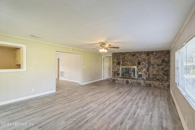 unfurnished living room with ceiling fan, crown molding, light hardwood / wood-style flooring, and a stone fireplace