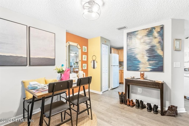 dining space featuring baseboards, a textured ceiling, visible vents, and light wood-style flooring