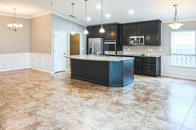 kitchen featuring appliances with stainless steel finishes, pendant lighting, light stone counters, ornamental molding, and a kitchen island with sink