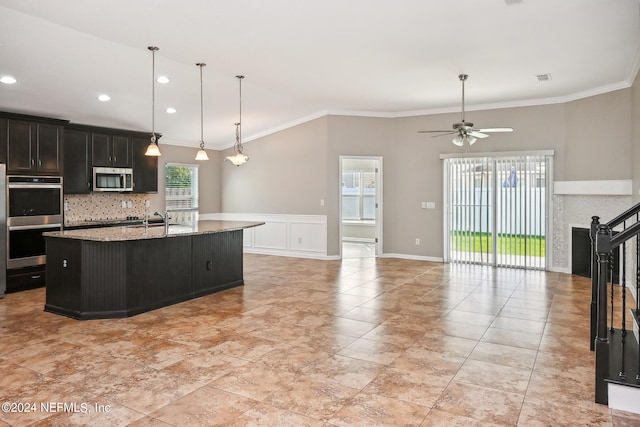 kitchen featuring light stone counters, ceiling fan, stainless steel appliances, crown molding, and a center island with sink