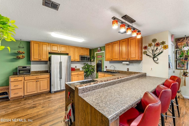 kitchen with light wood-type flooring, a textured ceiling, kitchen peninsula, hanging light fixtures, and appliances with stainless steel finishes