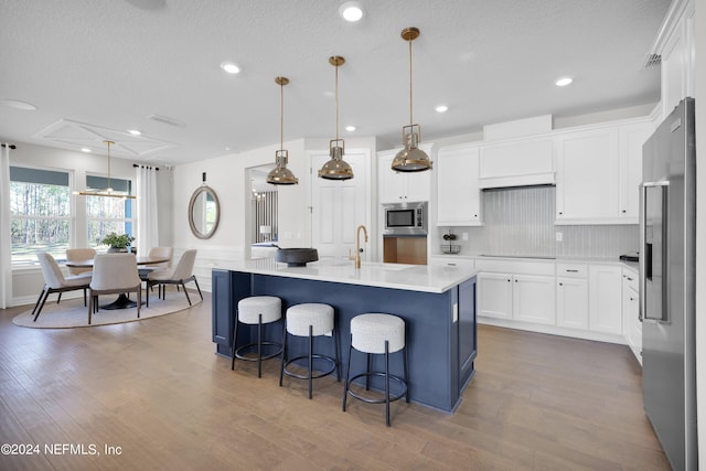 kitchen with pendant lighting, hardwood / wood-style flooring, an island with sink, white cabinets, and appliances with stainless steel finishes