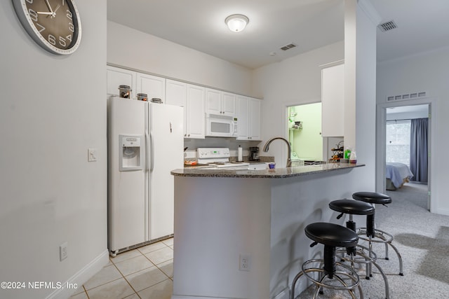 kitchen with light tile patterned flooring, white appliances, a breakfast bar area, kitchen peninsula, and white cabinets