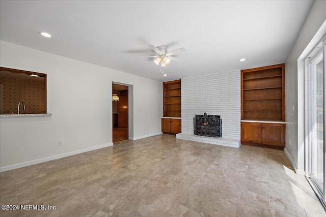 unfurnished living room featuring plenty of natural light, ceiling fan, sink, and a brick fireplace