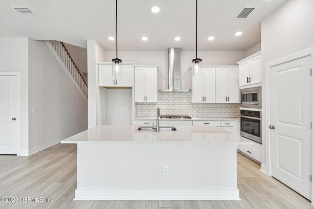 kitchen featuring wall chimney range hood, visible vents, appliances with stainless steel finishes, tasteful backsplash, and a sink