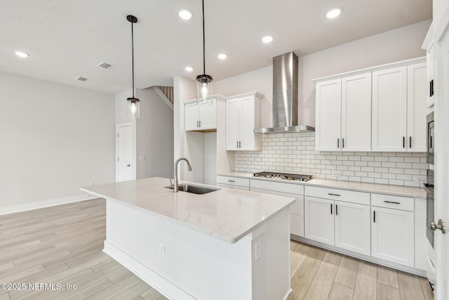kitchen with wall chimney range hood, a sink, light wood-style floors, white cabinetry, and decorative backsplash
