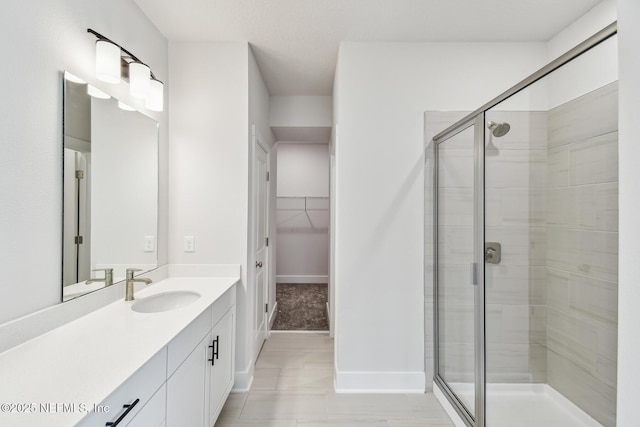 full bath with vanity, a walk in closet, baseboards, and a shower stall