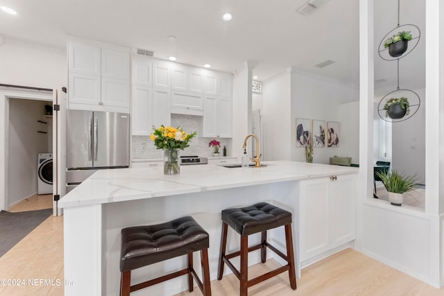 kitchen with sink, white cabinets, a kitchen bar, stainless steel fridge, and washer / dryer